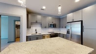 Located at 1331 Chester Ave in Raleigh's 27608 zip code, this single-floor residence showcases a clean, contemporary design throughout. The open-concept kitchen serves as the heart of the space, featuring flat-front gray cabinetry, a white subway tile backsplash, and a generously sized granite-topped island with pendant lighting overhead. Stainless steel appliances — including a refrigerator with ice maker, gas range, built-in microwave, and dishwasher — complement the modern aesthetic, while a matte black faucet adds a refined finishing touch. Light-toned hardwood flooring runs seamlessly throughout the unit, enhancing the bright and airy atmosphere. The bedrooms are well-proportioned, each with large windows that allow natural light to fill the rooms; one features a ceiling fan. The bathrooms offer a consistent design language, with one showcasing a walk-in glass shower with white tile surround, and another with open built-in shelving for added storage. A dedicated in-unit laundry closet houses a full-size washer and dryer. The hallway leads directly to an outdoor area, providing convenient access to the exterior. Gray interior doors with black hardware add a polished, cohesive touch throughout the home.