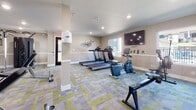 This well-appointed fitness center in El Cajon, CA offers a comprehensive workout environment spread across a single-level layout. The space features a vibrant design with bold green accent walls, neutral gray tones, white chair-rail molding, and a distinctive patterned carpet in shades of gray, green, and yellow that ties the room together cohesively.

The cardio zone is equipped with multiple treadmills, a Life Cycle recumbent bike, a Concept2 rowing machine, and a RowERG rower, complemented by a wall-mounted flat-screen television and a large window that brings in natural light and views of the surrounding outdoor area. A sanitizing station is conveniently positioned near the entrance.

The free weights area features a full rack of dumbbells, adjustable benches, and a medicine ball station, all set against floor-to-ceiling mirrors framed by glass panels that amplify the sense of space and allow for easy form checks. A Life Fitness cable machine provides additional strength training options in a dedicated alcove with clean, neutral-toned walls.

Recessed lighting throughout ensures bright, even illumination across all workout zones. A motivational "FITNESS" wall graphic adds an energetic touch to the space. The overall ambiance is modern, functional, and inviting — designed to support a full range of fitness activities.