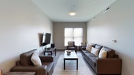 Located at 15 E Lane Ave in Columbus, Ohio, this single-floor unit offers a thoughtfully designed layout with modern finishes throughout. The living room serves as the centerpiece of the space, featuring warm hardwood-style flooring, neutral taupe walls, and large windows fitted with blinds that invite abundant natural light. The room comfortably accommodates multiple seating areas centered around a wall-mounted flat-screen TV, creating an inviting space for relaxing or entertaining.

The kitchen is outfitted with contemporary gray cabinetry, light granite-style countertops, a tile backsplash, and a full suite of stainless steel appliances including a range, microwave, and refrigerator. An in-unit washer is also conveniently accessible just off the kitchen.

Multiple bedrooms provide comfortable accommodations, each carpeted and featuring windows with natural light. The bedrooms offer sufficient space for a bed and a dedicated study area with a desk, making them well-suited for both rest and productivity.

Two bathrooms serve the unit — one featuring a full tub-shower combination with a clean white surround, and a second half-bath with a vanity, large mirror, and tile accent wall. Both bathrooms continue the modern aesthetic with wood-look flooring and neutral color palettes. Overall, the unit presents a clean, functional, and contemporary living environment.