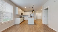 This well-designed single-floor residence offers a thoughtful layout that balances open living spaces with comfortable private areas. The heart of the home is the open-concept kitchen, which showcases crisp white cabinetry, a subway tile backsplash, dark countertops, and a full suite of stainless steel appliances including a refrigerator, range, and microwave. A central island provides additional prep space and seating, while three sleek black pendant lights with warm metallic accents add a contemporary design touch. Wood-look flooring flows throughout the main living areas, and large windows fitted with horizontal blinds allow ample natural light to fill the space.

The bedrooms are carpeted for comfort, each featuring windows with outdoor views and generous proportions. The primary bedroom is paired with an en-suite bathroom that includes a walk-in glass shower, a white vanity with undermount sink, and direct access to a spacious walk-in closet with built-in shelving and hanging rods. A secondary bathroom mirrors the clean aesthetic with a combination tub and shower, white cabinetry, and wood-look tile flooring. Black hardware accents throughout tie the modern design together cohesively, creating a fresh and unified aesthetic across every room.