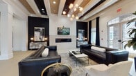 This upscale clubhouse is thoughtfully designed across a single floor, offering a series of interconnected social and recreational spaces unified by a refined black-and-white aesthetic with gold accents. The main lounge area commands attention with soaring ceilings, exposed dark wood ceiling beams set against white panels, and a striking sputnik-style chandelier. A sleek linear fireplace anchored by a stone surround serves as the focal point, flanked by bold black accent walls adorned with curated artwork. Black leather sofas, layered area rugs, and sculptural décor complete the sophisticated atmosphere.

The space flows seamlessly into a games room featuring a classic billiards table beneath an industrial-style pendant light, with large windows framing views of an outdoor pool and patio. A fully equipped wet bar area includes granite countertops, dark cabinetry, stainless steel mini-refrigerators, and a mounted television. A cozy lounge nook showcases a dramatic black paneled wall with a large-scale painting, while a smaller flex space with hardwood flooring and natural light offers an intimate seating area. Throughout, large windows dressed in navy drapes allow abundant natural light to fill every corner.