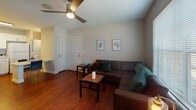 Located at 1101 Luther St W in College Station, TX, this single-floor unit offers a functional and comfortable layout designed for everyday living. Rich hardwood-style flooring flows through the main living areas, adding warmth and cohesion to the space.

The living room is a welcoming area featuring a ceiling fan with light fixture, large windows that invite natural light and outdoor views, and a sliding glass door that further brightens the room. The space comfortably accommodates a sectional sofa arrangement with room for additional seating and a coffee table.

The kitchen is well-equipped with white cabinetry offering generous storage, a full suite of appliances including an electric range, microwave, dishwasher, and refrigerator, along with a sink and ample counter space. A dining area adjacent to the kitchen provides space for a table and chairs, making it ideal for meals and casual gatherings.

The bedroom is a quiet, carpeted retreat with a ceiling fan, a sliding mirrored closet, and neutral walls that create a calm atmosphere. The full bathroom features a tub-shower combination, a single vanity with a wide mirror, and hardwood-style flooring consistent with the rest of the unit.

Overall, the space presents a clean, practical design well-suited for comfortable day-to-day living.