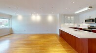 Located at 1443 Beacon Street in Brookline, MA, this single-floor residence combines modern finishes with a clean, functional layout. Warm hardwood flooring extends throughout the living areas and bedrooms, lending a cohesive and polished aesthetic to the entire space.

The kitchen is a standout feature, designed with two-toned cabinetry — rich mahogany-stained lower cabinets paired with crisp white upper cabinets, including glass-front display cases. White quartz countertops provide generous workspace, and stainless steel appliances, including a range, microwave, and refrigerator, complete the modern setup. A large island with an integrated sink defines the open connection between the kitchen and the adjacent living and dining area, which is illuminated by recessed and track lighting.

The living area offers an expansive, open feel with crown molding accents and multiple windows that bring in natural light and views of the surrounding Brookline streetscape. The bedrooms continue the hardwood flooring and feature large windows with views of the neighborhood's tree-lined streets and brick architecture.

The bathroom is well-appointed with neutral tile flooring, white cabinetry with ample storage on both sides, beige countertops, and a combined tub and shower. Throughout the unit, built-in shelving and thoughtfully placed closets provide practical storage solutions.