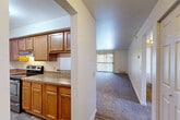 Located at 5800 Benson Dr in Haslett, Michigan, this 2-bedroom, 1-bathroom residence offers a practical and comfortable single-floor layout. The kitchen is well-appointed with warm honey-toned wood cabinetry, granite-style countertops, stainless steel appliances including an electric range and dishwasher, and wood-look vinyl flooring. It opens toward the living area via a pass-through design, creating a connected feel between the two spaces. The living room is generously sized, featuring plush carpeting and a sliding glass door with vertical blinds that leads to a private balcony, allowing for natural light and outdoor access. Both bedrooms are carpeted and fitted with ceiling fans, offering a comfortable and airy atmosphere. The primary bedroom is notably spacious, with a large window that brings in natural light and views of surrounding greenery. The second bedroom also features built-in shelving. Three closets throughout the unit provide ample storage. The bathroom includes a full tub-shower combo with white tile surround, a vanity with wood cabinetry, and wood-look flooring. Two hallways connect the rooms, contributing to an efficient and well-organized floor plan throughout this Haslett residence.