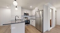Located at 458 Parker Ave in Philadelphia's Roxborough neighborhood, this thoughtfully designed one-bedroom, one-bathroom unit offers a clean, modern aesthetic across a well-utilized single floor. Light-toned hardwood-style flooring flows throughout, complementing the bright white walls and recessed lighting that keep the space feeling open and airy.

The combined kitchen and living area serves as the heart of the unit. The kitchen is outfitted with white shaker cabinetry, a white subway tile backsplash, dark granite countertops, and a full suite of stainless steel appliances including a refrigerator, range, and over-the-range microwave. A peninsula with pendant lighting provides additional prep space and casual seating potential. A stacked washer and dryer is conveniently tucked behind a dedicated closet door nearby.

The bedroom is a comfortable, well-proportioned room featuring a window with natural light, a wall-mounted thermostat, and direct access to a dedicated walk-in closet with built-in shelving.

The bathroom features large-format grey floor tile, a soaking tub with full hexagonal tile surround, matte black fixtures, and a warm wood-toned vanity with a white countertop — a refined blend of modern and natural materials throughout.
