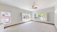 This one-bedroom, one-bathroom residence is thoughtfully laid out across a single floor, offering an efficient and comfortable living environment. The open living room is a standout feature, bathed in abundant natural light streaming through multiple large windows that frame views of tree-lined streets and the surrounding urban neighborhood. A ceiling fan adds to the room's comfort, and neutral carpet flooring lends a clean, inviting feel throughout the living and sleeping areas.

The kitchen is well-equipped with light wood cabinetry, ample overhead storage, a full-size refrigerator, an electric range, and a sink with countertop workspace. Wood-style flooring runs through the kitchen, complementing the warm cabinetry tones. A half-wall peninsula separates the kitchen from the living area, creating a natural flow between spaces.

The bedroom offers a generous footprint with large windows providing greenery views and plenty of natural light. It includes a closet with a rod and shelving system, along with additional storage accessible through a nearby secondary closet with built-in shelving.

The bathroom features a vanity with a sink and mirror, a toilet, and wood-style flooring. Neutral gray walls and white trim throughout the residence create a cohesive, modern aesthetic. The overall ambiance is bright, clean, and functional.