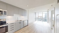Located in the heart of downtown San Diego at 1150 E Street, this modern 1-bedroom, 1-bathroom residence offers a sleek, contemporary design throughout. Light-toned hardwood-style flooring runs seamlessly across the open-plan layout, complementing the bright, airy atmosphere created by abundant natural light. The combined kitchen and living area forms the centerpiece of the space, featuring a well-appointed kitchen with flat-front gray cabinetry extending to ceiling height, a white tile backsplash, stainless steel appliances including a refrigerator, range, microwave, and dishwasher, and a undermount sink. The open living area flows effortlessly toward dramatic floor-to-ceiling windows that frame sweeping views of the San Diego skyline and cityscape beyond. The bedroom is generously bathed in natural light, with its own large window wall offering equally impressive city views. The bathroom is finished in a modern style, featuring a floating vanity with a mirrored medicine cabinet, contemporary fixtures, and clean tile flooring. A dedicated closet provides practical storage, while a private balcony extends the living space outdoors, offering direct access to panoramic urban views. Recessed lighting throughout completes the clean, polished aesthetic of this well-designed residence.