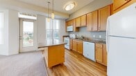 Located at 3700 Huset Pkwy NE in Columbia Heights, Minnesota, this single-floor residence offers a thoughtfully designed layout with a clean, modern aesthetic. The entryway opens into a hallway finished with durable hardwood-style flooring, providing a welcoming transition into the main living areas. The kitchen serves as a functional centerpiece, featuring warm maple cabinetry, granite countertops, a central island ideal for meal preparation or casual dining, and white appliances including a range, microwave, dishwasher, and refrigerator. Pendant lighting accents the space, while large windows flood the kitchen with natural light and offer views of the surrounding neighborhood. The living areas are carpeted in neutral tones and benefit from an abundance of natural light courtesy of expansive windows dressed with vertical blinds. The spacious bedrooms continue the same neutral palette and plush carpeting, with generously sized windows framing outdoor views. The bathrooms are well-equipped, featuring warm wood cabinetry, wide vanities with ample counter space, large mirrors, and hardwood-style flooring. One bathroom includes a walk-in shower with safety grab bars. Throughout the residence, the consistent use of light tones and natural materials creates a cohesive, inviting atmosphere.