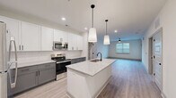 Located at 1130 Annondale Dr in Fayetteville, NC, this well-designed one-bedroom, one-bathroom residence offers a thoughtful layout across a single floor. The open-concept kitchen serves as the heart of the home, showcasing a central island with a granite countertop and undermount sink, elegant pendant lighting with matte black accents, and a two-tone cabinet scheme pairing crisp white upper cabinets with gray lower cabinets. A subway tile backsplash and a full suite of stainless steel appliances — including a refrigerator, electric range, microwave, and dishwasher — complete the kitchen. The kitchen flows seamlessly into the living room, which features light wood-tone luxury vinyl plank flooring, a ceiling fan, and natural light from windows fitted with blinds. The bedroom is a comfortable, well-proportioned retreat with its own ceiling fan, natural light, and easy access to a walk-in closet outfitted with wire shelving on multiple walls for generous storage. The bathroom features a large glass-enclosed shower with a rain showerhead and matte black hardware, complementing the clean, modern aesthetic found throughout. Light, neutral tones and consistent flooring create a cohesive and contemporary ambiance throughout the entire space.