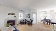 This single-floor residence offers a thoughtfully designed layout with a bright, open ambiance throughout. The living room serves as the heart of the home, featuring a tile-surround fireplace, plush wall-to-wall carpeting, and large windows dressed with sheer curtains that fill the space with natural light. A sliding glass door opens to an outdoor area, extending the living space beyond the interior. Adjacent to the living room, a dedicated dining area provides a comfortable setting for meals.

The kitchen is well-equipped with white cabinetry, light stone-toned countertops, a full suite of white appliances including a refrigerator and range, and durable hardwood-style flooring. Ample cabinet storage and counter space make this a highly functional cooking area.

The bedrooms are carpeted and generously sized, each featuring ceiling fans with lighting. The primary bedroom benefits from direct access to a connected bathroom, which includes a wide vanity with a speckled countertop, a large mirror with overhead lighting, and clean white finishes throughout.

A secondary bathroom provides a private water closet. The overall color palette of crisp whites and soft neutrals creates a clean, cohesive aesthetic, making this a comfortable and inviting space.