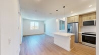 Located at 1151 Encanto Loop in Chula Vista, CA, this well-designed two-bedroom, two-bathroom residence offers a clean, contemporary aesthetic across its thoughtfully laid-out floor plan. Light wood flooring flows seamlessly throughout, complementing the bright white walls and modern finishes that define the space.

The open-concept kitchen and living area serves as the heart of the home. The kitchen is outfitted with warm wood cabinetry, a white quartz countertop island with pendant lighting, a stylish geometric tile backsplash, and stainless steel appliances including a gas range, microwave, and refrigerator. The adjacent living area is bathed in natural light from large windows with views of the surrounding neighborhood.

Both bedrooms are well-proportioned and bright, featuring large windows, light wood flooring, and clean white walls. The primary bedroom includes a generous walk-in closet with wire shelving for ample storage. A second closet provides additional organization space elsewhere in the home.

The two bathrooms are finished with wood-toned vanity cabinetry, white quartz countertops, and light flooring. One bathroom features a full tub-shower combination with white subway tile surround. A private balcony extends the living space outdoors, offering additional room to relax and enjoy the Southern California climate.