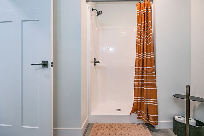 Baño moderno con una elegante ducha con una cortina de rayas naranjas, complementada con una elegante repisa de almacenamiento y un diseño de puerta contemporáneo. - Orchard on Wallen