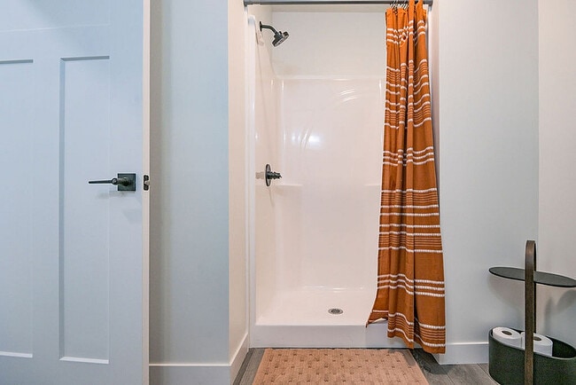 Modern bathroom featuring a sleek shower with an elegant orange stripe curtain, complemented by a stylish storage shelf and a contemporary door design. - Orchard on Wallen