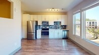 Located at 930 Jones Franklin Rd in Raleigh, NC, this single-floor unit offers a well-designed layout with modern finishes throughout. The kitchen is a standout feature, showcasing crisp white shaker-style cabinetry extending to the ceiling for generous storage, complemented by a slate-blue subway tile backsplash and stainless steel appliances including a refrigerator, electric range, built-in microwave, and dishwasher. Track lighting and a large window flood the kitchen with natural light, while wood-look plank flooring ties the space together seamlessly into the open living area. The living space is airy and bright, featuring a ceiling fan with a brushed gold finish and additional windows that invite natural light. A recessed niche adds a subtle architectural detail to the room. The bathroom is finished with elegant marble-look porcelain tile flooring, a white vanity with clean-lined cabinetry, a wall-mounted light fixture above a framed mirror, and a toilet — all presented in a crisp, neutral palette. The overall ambiance of the unit is clean, contemporary, and move-in ready, reflecting thoughtful design choices suited for comfortable everyday living in the Raleigh area.
