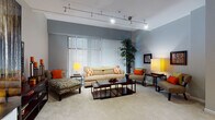 Located on Euclid Avenue in the heart of Cleveland, Ohio, this single-floor residence offers a well-designed layout with thoughtfully appointed living spaces throughout. The expansive living room serves as the centerpiece of the home, featuring soft carpeting, cool gray walls, and track lighting overhead. Large floor-to-ceiling vertical blinds allow for generous natural light while providing privacy, and the room comfortably accommodates multiple seating arrangements, making it ideal for both relaxing and entertaining. A dedicated sitting nook with striped accent chairs and a side table adds an additional layer of functionality to the living area. The kitchen is outfitted with warm natural wood cabinetry, rich dark granite countertops, a slate tile backsplash, and stainless steel appliances, including a dishwasher and range. Light tile flooring completes the clean, functional aesthetic. The bedrooms are carpeted and serene, each featuring ceiling fans, ample closet space with organized shelving, and room for a substantial bed frame with nightstands. The bathroom is finished with beige and navy tile work, a glass-enclosed walk-in shower, and cabinetry consistent with the kitchen's design language. Throughout the residence, a cohesive warm-toned color palette ties each room together seamlessly.