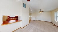 This two-story home is thoughtfully laid out across two floors, offering a comfortable and functional living environment. The main floor houses the living room and kitchen, while the upper floor accommodates both bedrooms and bathrooms. The living room is a standout feature, showcasing soaring vaulted ceilings with a ceiling fan, plush carpeting, and ample natural light streaming through multiple windows. A half-wall partition visually connects the living area to the kitchen, which features warm honey-toned wood cabinetry, bold red countertops, light wood-style flooring, and a full suite of appliances including a range, dishwasher, and refrigerator. A carpeted staircase with a classic wood handrail leads to the upper floor, where two hallways connect the bedrooms and bathrooms. Each bedroom offers soft carpet, closet storage, and warm neutral tones. One bedroom features a walk-in closet with a vaulted ceiling detail. The bathrooms are clean and functional, with one featuring a tub-shower combo with sliding glass doors and wood-style flooring. Throughout, warm wood-toned doors and trim provide a cohesive, inviting aesthetic.