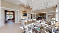 This generously sized single-floor amenity space is thoughtfully designed across three distinct areas, combining modern aesthetics with functional versatility. The main lounge area serves as the centerpiece, featuring soaring ceilings adorned with a striking sculptural wood slat installation that extends overhead, complementing a sleek white bar counter lined with modern bar stools. Recessed lighting and elegant pendant fixtures illuminate the open-plan layout, while large windows flood the space with natural light and offer outdoor views. Comfortable seating arrangements with curated furnishings and layered area rugs create an inviting social atmosphere.

The game room offers a dramatic setting with double-height ceilings, large windows with floor-length drapes, and a statement pool table anchored beneath a cluster of cylindrical glass pendant lights. A built-in wood-paneled media wall with dual flat-screen televisions adds an entertainment focal point, while patterned carpet tiles define the play area.

A dedicated coworking zone provides workstations along light wood cabinetry, a sculptural lattice room divider, and glass-paneled private rooms. A separate service corridor features continuous quartz countertops, warm wood cabinetry, and decorative slatted ceiling details, connecting the areas cohesively throughout.