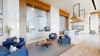 The Morning Room in Denver, Colorado is a generously sized, single-floor communal space that seamlessly blends contemporary design with welcoming comfort. Soaring ceilings create an expansive, airy atmosphere throughout, while extensive floor-to-ceiling curtain-wall glazing floods the interior with abundant natural light and frames sweeping views of the surrounding Denver streetscape and outdoor courtyards.

Light-toned tile and wood-plank flooring extend across the entire space, complemented by warm slatted wood ceiling panels that add texture and visual warmth. The living area is organized into several distinct seating zones, each thoughtfully furnished — from leather lounge sofas and tailored upholstered armchairs to a striking live-edge resin coffee table that serves as a natural focal point.

A built-in beverage and service station, finished in soft white cabinetry with a textured stone backsplash, occupies one wall and is accompanied by a sleek bar counter with high seating. A sculptural geometric chandelier adds an artistic accent overhead. A linear fireplace integrated into a polished wall panel provides an intimate corner retreat alongside large windows overlooking the tree-lined exterior.

The hallway connects seamlessly to the main lounge, with a dramatic backlit feature wall of illuminated grid panels providing a bold architectural statement. The overall ambiance is refined, light-filled, and modern.
