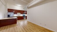 Located at 2013 Ontario St in Cleveland, OH, this one-bedroom, one-bathroom unit offers a well-organized single-floor layout with a functional and stylish design. The open living and kitchen area is the heart of the space, featuring warm hardwood-style flooring that runs throughout. The kitchen is outfitted with rich cherry-toned cabinetry, granite countertops, a stainless steel range, microwave, and dishwasher. A kitchen island with a granite surface and pendant lighting above adds both prep space and a casual dining option. Exposed ceiling pipes and ductwork lend a subtle industrial character to the living area, complemented by clean white walls and a wood-accented entry door with a glass panel that allows natural light into the main room. The bedroom is a cozy, well-proportioned space with a double-door closet for ample storage and a window overlooking the exterior. Light hardwood flooring continues here, maintaining a cohesive feel. The bathroom features a full soaking tub and shower combination, surrounded by large-format neutral tiles accented by a decorative mosaic border in earthy tones, finished with brushed gold fixtures. A hallway connects the rooms efficiently, completing this compact yet thoughtfully designed urban residence.