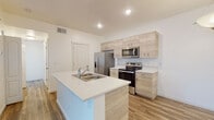 This single-floor residence at 9601 W State St in Garden City, Idaho, offers a clean, modern aesthetic throughout its thoughtfully designed layout. The interior is characterized by a neutral color palette of crisp whites and warm wood tones, creating a bright and cohesive atmosphere across all rooms.

The kitchen serves as a central highlight, featuring light wood cabinetry extending to the upper walls, white quartz countertops, and a full suite of stainless steel appliances including a refrigerator with ice maker, electric range, and over-the-range microwave. A peninsula island with an integrated sink provides additional workspace and separates the kitchen from the adjoining dining area, which is illuminated by a pendant light fixture. Wood-look luxury vinyl flooring flows throughout the main living areas, enhancing the warm, contemporary feel.

The living room offers a generous open layout with a sliding glass door that draws in natural light. The bedroom is finished with plush carpeting and features multiple windows with blinds for privacy. The bathroom maintains the home's modern character with light wood vanity cabinetry, wood-look flooring, and a window for natural ventilation. A dedicated laundry area accommodates a full-size washer and dryer alongside built-in shelving for added storage convenience.