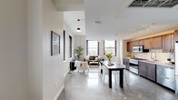 This single-floor urban residence blends contemporary design with industrial-inspired touches throughout. The open-plan layout seamlessly connects the living, dining, and kitchen areas, all anchored by polished concrete floors that reflect natural light pouring in through oversized black-framed windows. These striking windows frame sweeping city skyline views, creating a dynamic urban backdrop in both the living and bedroom spaces.

The kitchen is appointed with rich dark wood cabinetry, white subway tile backsplash, light stone countertops, and a full suite of stainless steel appliances including a professional gas range, built-in microwave, dishwasher, and French door refrigerator. Track lighting overhead ensures excellent task illumination throughout.

The living area offers generous proportions with room for both a seating arrangement and a dining table, with the city views serving as a natural focal point. The bedroom provides a quieter retreat, featuring dual closets and exposed ductwork that nods to the building's industrial character. A dedicated home office space includes a rustic wood desk and neutral walls ideal for focused work.

Two bathrooms complete the layout: a full bath with a subway-tiled walk-in shower and single vanity, and a second bath featuring a tiled shower-over-tub combination with glass enclosure and dark stone countertop vanity.
