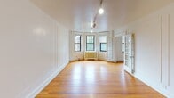 Located at 5515 Wissahickon Ave in Philadelphia's 19144 neighborhood, this single-floor residence combines classic architectural character with functional design throughout. Warm hardwood floors flow consistently through the living areas and bedrooms, complementing the crisp white walls and decorative panel molding that lend a refined, traditional aesthetic to each room.

The spacious living room is a standout feature, showcasing a bay window that frames natural greenery and fills the space with abundant natural light. Elegant French doors connect the living room to an adjoining room, which is equipped with track lighting — ideal for flexible use. Ceiling fans are present in multiple rooms, enhancing comfort throughout.

The bedrooms are well-proportioned, each featuring hardwood floors, ceiling fans, and panel-detailed walls. One bedroom includes built-in closets framed with classic millwork, providing ample storage. Radiator heating units are present in several rooms, characteristic of the building's traditional construction.

The kitchen offers generous cabinetry in warm oak tones, a butcher block-style countertop, and light tile flooring, providing a practical and welcoming cooking space. The bathroom retains its classic charm with white subway tile wall cladding, hexagonal floor tile, a full bathtub, and a window for natural ventilation. The overall ambiance is clean, bright, and timeless.