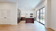 Located at 3604 Rainbow Blvd in Kansas City, KS, this thoughtfully designed one-bedroom, one-bathroom unit offers a contemporary living experience across a single floor. The open-concept layout is anchored by a well-appointed kitchen featuring a two-tone cabinet design — crisp white upper cabinets paired with rich dark wood lower cabinets — complemented by a white quartz-topped center island, stainless steel appliances including a refrigerator, range, microwave, and dishwasher, and a clean subway tile backsplash. Light wood-style flooring extends throughout the main living areas, enhancing the bright, airy atmosphere created by recessed lighting and large sliding glass doors that open to a private balcony with outdoor views. The hallway connects the living spaces to a dedicated closet with louvered doors and a cozy carpeted bedroom with tall ceilings, offering a calm retreat. The bathroom is elegantly finished with marble-look floor and wall tiles, a soaking tub-shower combination, brushed nickel fixtures, and a dark wood vanity with a white countertop. Clean white walls and modern black door hardware throughout contribute to the unit's cohesive, contemporary aesthetic.