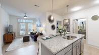 Located at 2050 Stanford Ln in Newport News, VA, this 2-bedroom, 2-bathroom residence offers a thoughtfully designed single-floor layout that maximizes comfort and functionality. The open-concept living and kitchen area serves as the heart of the home, where light hardwood-style flooring flows seamlessly between spaces. The kitchen is outfitted with sleek gray shaker cabinets, granite countertops, a large peninsula with an undermount sink, stainless steel appliances including a range, microwave, and refrigerator, and stylish pendant lighting overhead. The living room features a ceiling fan, neutral walls, and French doors with transom windows that invite natural light and provide direct access to a private outdoor area. Both bedrooms are carpeted and bright, with ceiling fans and windows dressed with blinds and curtains. The primary bedroom includes a walk-in closet with wire shelving systems, offering ample storage. The bathrooms are clean and functional, with one featuring a glass-enclosed shower with white tile surround. Two dedicated closets throughout the home further enhance storage. The overall ambiance is bright, modern, and inviting, making this a practical and attractive residence in Newport News.