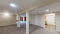 Located at 91 Elm St in Manchester, Connecticut, this two-story residence offers a distinctive blend of industrial character and residential comfort. The main floor is the larger of the two levels and immediately impresses with dramatic soaring ceilings, exposed brick walls, and soft carpeting underfoot. The spacious primary bedroom showcases these standout architectural elements, including a large closet and an open, airy feel enhanced by the tall ceilings. The galley-style kitchen is well-appointed with warm wood cabinetry lining both sides, a gas range, a full-size refrigerator, and light wood-look flooring, providing ample storage and counter space. The bathroom is finished with wood-plank ceiling detail, wood vanity cabinetry, tile-look flooring, and a full tub-shower combination. The second floor features a second bedroom with a charming natural wood plank ceiling and exposed beams, adding warmth and rustic character, along with its own closet. The basement level provides additional flexible space with carpeting and industrial-style pipe detailing along the ceiling. Throughout the home, the interplay of exposed brick, wood ceilings, and neutral tones creates a warm yet characterful ambiance that is both unique and inviting.