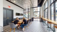 Located at 205 S High St in the heart of downtown Columbus, Ohio, this single-floor commercial space blends classic architectural charm with modern design sensibilities. The interior immediately draws the eye upward to its stunning embossed tin ceiling, a standout feature that adds elegance and a nod to historic craftsmanship. Underfoot, bold black-and-white geometric patterned tile flooring creates a striking visual contrast and anchors the space with a strong design identity.

Large floor-to-ceiling windows line the street-facing wall, inviting an abundance of natural light and offering open views of the surrounding urban streetscape. The bright, airy atmosphere is complemented by high ceilings that enhance the sense of openness throughout. Dark wainscoting along the lower walls adds depth and a refined finish to the interior.

The space is thoughtfully appointed with a mix of communal wooden tables, upholstered seating, and bar-height counter seating along the windows — well-suited for collaborative work, meetings, or casual gatherings. Wall-mounted displays add a functional, modern touch. The overall ambiance is contemporary yet characterful, making this a versatile and visually compelling space ideally situated in one of Columbus's most vibrant commercial corridors.