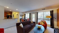 This single-story residence offers a thoughtfully designed layout that balances comfort and functionality across its main living spaces. The living room serves as the heart of the unit, featuring large sliding glass doors and expansive windows that flood the area with natural light and provide views of the surrounding outdoor space. Neutral carpet flooring and clean white ceilings contribute to a bright, open atmosphere throughout.

Adjacent to the living area, the dining space accommodates a round table and chairs, positioned directly beside a large window that maintains the home's connection to the outdoors. A dark wood sideboard provides additional storage and display space.

The kitchen is well-appointed with warm cherry wood cabinetry reaching toward the ceiling, granite-style countertops, and a full suite of black appliances including a range, microwave, dishwasher, and refrigerator. Light tile flooring completes the practical, clean aesthetic.

The bedroom is generously proportioned, featuring plush carpet, a ceiling fan, a sage green accent wall, and a window allowing natural light to filter in. A hallway bathroom features an extended vanity with medium-toned wood cabinetry, a wide mirror, and tile flooring, offering ample counter and storage space.