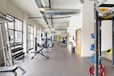 Located at 1111 Hawthorne Lane in Charlotte's Plaza Midwood neighborhood, this fitness facility offers a thoughtfully designed, two-room exercise space spread across a single floor. The design masterfully blends historic character with modern functionality, featuring striking exposed brick and stone accent walls alongside crisp white surfaces and soaring ceilings with visible ductwork — a hallmark of industrial-chic architecture.

The main exercise room is bathed in natural light streaming through large floor-to-ceiling windows that frame views of the surrounding brick building exterior and an outdoor pool area. This generously proportioned space is outfitted with a full row of treadmills, cable machines, strength equipment, a smith machine, flat bench, dumbbell rack, and a heavy punching bag — catering to a wide range of fitness routines. Pendant lighting and exposed ceiling conduits add to the loft-inspired aesthetic.

The second exercise room provides a dedicated functional training zone, featuring a multi-station rig with TRX suspension trainers and battle ropes, a floor-to-ceiling mirror wall, spin bikes, stability balls, medicine balls, and a power tower. Durable rubber flooring runs throughout both rooms, ensuring comfort and safety. Together, the two rooms form a comprehensive, well-appointed fitness destination with character and substance.