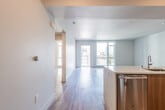 This contemporary single-floor residence offers a thoughtfully designed open-concept layout with clean lines and modern finishes throughout. Durable light wood-tone flooring runs continuously across the living, dining, and kitchen areas, creating a cohesive and inviting atmosphere.

The kitchen serves as a functional centerpiece, featuring a large island with a quartz countertop, an undermount sink, and warm wood cabinetry contrasted by crisp white upper cabinets. A glossy subway tile backsplash adds texture, while a full suite of stainless steel appliances — including a gas range, over-the-range microwave, and French door refrigerator — completes the space.

The open living area is generously proportioned and bathed in natural light from large floor-to-ceiling windows and a glass balcony door, which frames outdoor urban and mountain views. An additional bedroom benefits from its own oversized window with city views, filling the room with abundant daylight.

The primary bathroom features a glass-enclosed walk-in shower with grey subway tile, a wood-toned vanity with a white countertop, and a large mirror. A second full bathroom offers a soaking tub with a matching grey tile surround, built-in shelving, and hardwood-style flooring. Together, these spaces reflect a cohesive, contemporary design sensibility throughout.
