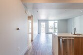 This contemporary single-floor residence offers a thoughtfully designed open-concept layout with clean lines and modern finishes throughout. Durable light wood-tone flooring runs continuously across the living, dining, and kitchen areas, creating a cohesive and inviting atmosphere.

The kitchen serves as a functional centerpiece, featuring a large island with a quartz countertop, an undermount sink, and warm wood cabinetry contrasted by crisp white upper cabinets. A glossy subway tile backsplash adds texture, while a full suite of stainless steel appliances — including a gas range, over-the-range microwave, and French door refrigerator — completes the space.

The open living area is generously proportioned and bathed in natural light from large floor-to-ceiling windows and a glass balcony door, which frames outdoor urban and mountain views. An additional bedroom benefits from its own oversized window with city views, filling the room with abundant daylight.

The primary bathroom features a glass-enclosed walk-in shower with grey subway tile, a wood-toned vanity with a white countertop, and a large mirror. A second full bathroom offers a soaking tub with a matching grey tile surround, built-in shelving, and hardwood-style flooring. Together, these spaces reflect a cohesive, contemporary design sensibility throughout.