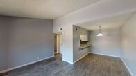 This single-floor residence offers a clean, contemporary layout designed for comfortable everyday living. The open living and dining area is finished with durable wood-look plank flooring and neutral gray walls, creating a cohesive and modern aesthetic throughout. Textured ceilings add a classic touch, while ample wall space provides flexibility for furnishing and décor.

The kitchen connects seamlessly to the dining area via a pass-through counter with a granite-style surface that doubles as a breakfast bar. White cabinetry, a mosaic tile backsplash in blue and gray tones, and an undermount sink complete the functional and stylish kitchen space. A pendant light overhead adds a warm accent.

The bedrooms are carpeted for comfort and feature large windows dressed with vertical blinds that allow natural light to filter in. One bedroom includes a sliding glass door opening to a private balcony with views of the surrounding exterior. The entry area is finished with the same wood-look plank flooring as the main living space.

The bathrooms are outfitted with white vanities topped with granite-style countertops, mirrored medicine cabinets, and a combined tub and shower unit with a curved curtain rod. Wood-look flooring continues into the bathrooms, tying the overall design together with a consistent, updated finish throughout the home.
