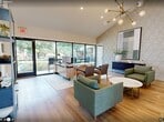Located at 320 East Wintergreen Road in DeSoto, Texas, this 590 square foot single-floor leasing office is thoughtfully designed with a modern aesthetic and functional layout across three distinct areas: an entrance, a living room, and a private office.

The entrance and living room area immediately impress with soaring vaulted ceilings, warm hardwood-style flooring, and a striking geometric textured accent wall that extends to the full height of the ceiling. A bold sputnik-style brass chandelier serves as a focal point, lending a mid-century modern character to the space. Comfortable green upholstered seating is arranged around a marble-top coffee table, creating a welcoming reception atmosphere. A compact kitchenette with open white shelving, a subway tile backsplash, stainless steel appliances, and a sink is tucked neatly into the corner.

The main office area features a large L-shaped wood-toned desk and floor-to-ceiling black-framed sliding glass doors that flood the space with natural light and offer direct views of an outdoor pool and lush tree-lined grounds. A dedicated computer workstation room provides a quiet workspace with dual monitors, a printer, built-in white cabinetry, and a decorative blue patterned accent wall. Together, these spaces create a polished, professional, and inviting environment.