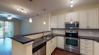 This single-floor residence offers a thoughtfully designed layout with a cohesive blend of functional and stylish finishes throughout. The open living area is finished with rich, dark hardwood-style flooring and crowned with elegant crown molding. A ceiling fan overhead provides comfort, while a sliding glass door floods the space with natural light and provides access to an outdoor area. The kitchen is a standout feature, showcasing white shaker-style cabinetry, dark granite countertops, and a full suite of stainless steel appliances including a double oven range, built-in microwave, refrigerator, and dishwasher. A breakfast bar peninsula offers additional counter space and a casual dining option, while pendant lighting and track lighting add a polished touch. The tile backsplash ties the kitchen together with a clean, classic look. The bedroom is carpeted for comfort, features a ceiling fan with a natural light window, and is accompanied by a walk-in closet outfitted with wire shelving and hanging rods for organized storage. The bathroom includes a full soaking tub and shower combo with white subway tile surround, brushed nickel fixtures, and grab bars, complemented by dark granite vanity countertops and hardwood-style flooring.