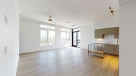 This single-floor residence in Carson, California presents a clean, modern aesthetic defined by bright white walls, light-toned hardwood flooring, and an open, airy layout. The spacious main living area is a standout feature, bathed in natural light through large windows and transom panels that frame views of the surrounding neighborhood and palm-lined skyline. A ceiling fan, track lighting, and a floor-to-ceiling glass door leading to a balcony further enhance the room's contemporary character.

The kitchen is well-appointed with taupe flat-front cabinetry, a white subway tile backsplash, stainless steel appliances including a range, dishwasher, and over-the-range microwave, and a portable stainless steel prep table for added workspace. Warm hardwood flooring ties the kitchen seamlessly into the living area.

The bedrooms feature neutral carpet, ceiling fans, and windows offering outdoor views, with one room including a sliding-door closet. Two bathrooms serve the unit: one features a soaking tub, single vanity, and gold-accented lighting, while the second offers a glass-enclosed walk-in shower and a wide double-sink vanity with light wood cabinetry and hardwood floors throughout.