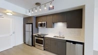 This single-floor residence offers a thoughtfully designed layout within a one-bedroom, one-bathroom floor plan. The kitchen serves as a standout feature, showcasing a sleek, modern aesthetic with dark espresso-toned cabinetry that extends to the ceiling, providing ample storage. Stainless steel appliances — including a full-size refrigerator, electric range, built-in microwave, and dishwasher — lend a professional, polished look. The white subway tile backsplash creates a clean contrast against the darker cabinetry, while light-toned countertops and a stainless steel undermount sink add functional elegance. Track lighting mounted on the ceiling illuminates the workspace effectively, enhancing both practicality and ambiance. Light wood-toned flooring runs throughout, contributing to a bright, airy feel that makes the space feel open. The overall design reflects a contemporary style with a neutral, cohesive color palette that balances modern hardware details with clean lines — creating a functional and visually appealing living environment suited to everyday comfort.