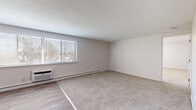 Located at 215 Fort Pleasant in Springfield, Massachusetts, this single-floor residence offers a practical and comfortable layout designed for everyday living. The spacious living area features plush wall-to-wall carpeting and hard-surface flooring at the entry transition, with large windows fitted with horizontal blinds that invite an abundance of natural light. A wall-mounted air conditioning unit and baseboard heating ensure year-round climate comfort throughout the main living spaces. The kitchen is equipped with a stainless steel electric range set against a stylish linear mosaic tile backsplash, complemented by wood-look flooring and light-toned countertops, creating a clean and modern cooking environment. The bedroom is generously sized, featuring soft carpeting, a closet, and direct access to a full bathroom. The bathroom is finished with classic white subway tile accented by dark border trim, and includes a full soaking tub with a glass sliding shower enclosure and chrome fixtures. A louvered closet door and built-in shelving add functional storage throughout. The neutral color palette, clean finishes, and well-proportioned rooms combine to create a bright, move-in-ready living environment.