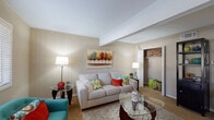 This single-story residence offers a well-organized layout designed for comfortable everyday living. The living room serves as the heart of the home, featuring distinctive vertical wood-panel accent walls, a vaulted ceiling with an exposed beam detail, and soft carpet underfoot. Natural light enters through a window fitted with white plantation shutters, complementing the warm, neutral color palette. An open closet nook visible from the living area adds practical storage.

The kitchen is efficiently arranged in a galley-style configuration, featuring tile flooring, dark countertops, taupe cabinetry, a coil-burner range, dishwasher, and a full-size refrigerator. Adjacent to the kitchen, the dining area benefits from additional natural light through a sizable window and is equipped with a ceiling fan overhead.

The bedroom is a calm retreat with plush carpet, neutral walls, a ceiling fan, and a window dressed with sheer curtains and blinds that allow ample daylight. A secondary room offers flexible use as a home office or sitting room, also featuring carpet, a ceiling fan, and a window. Throughout the residence, a consistent neutral tone, practical finishes, and natural light contribute to a cohesive and inviting atmosphere.