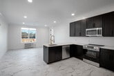 Located at 102 W Main St, this thoughtfully designed 2-bedroom, 3-bathroom unit offers a refined modern aesthetic across a single level. Marble-style tile flooring runs throughout, lending an elegant and cohesive feel to every room. The open-concept kitchen is a standout, featuring bold dark shaker cabinetry, a light quartz peninsula, stainless steel appliances including a refrigerator, range, microwave, and dishwasher, and a gold-accented faucet that adds a warm contrast to the contemporary palette. Recessed lighting illuminates the living and kitchen areas effectively. The bedrooms are bright and well-proportioned, with the primary bedroom offering a comfortable footprint and large windows that invite natural light and street views. Built-in closets provide practical storage. The three bathrooms are finished with care — highlights include white subway tile surrounds, matte black fixtures, marble-top vanities, illuminated round mirrors, and a glass-enclosed shower. A clean white corridor connects the rooms with a sense of flow and openness. Panel-style interior doors with black hardware add a modern touch throughout. The overall ambiance is clean, bright, and move-in ready.
