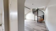 Located at 305 S Main St in Middletown, Connecticut, this two-floor space offers a well-designed layout with a range of functional and architectural highlights. The main level features light gray laminate flooring throughout, clean white walls, and an open feel enhanced by a standout spiral staircase with warm wood treads and a bold black metal railing — a defining architectural element that connects both floors with visual flair. The lower level includes a functional kitchen equipped with stainless steel appliances, including a full-size refrigerator and electric range, cream cabinetry with wood trim accents, and ample counter space. A full bathroom on this level offers a combination tub and shower, a wood-toned vanity with a white countertop, and light tile-style flooring. The upper floor is a bright, open loft-style area distinguished by soaring angled ceilings and a pair of skylights that flood the space with natural light. Baseboard heating is present throughout, ensuring year-round comfort. The overall aesthetic is clean and modern, with a neutral color palette that creates a versatile and inviting atmosphere suitable for a variety of uses.