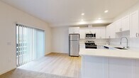 This single-floor residence offers a clean, contemporary design highlighted by a neutral color palette and a thoughtful layout visible in its 3D floor plan. The kitchen serves as a central feature, outfitted with white shaker-style cabinetry extending to the ceiling, light-toned countertops, and a full suite of stainless steel appliances including a refrigerator, gas range, over-the-range microwave, and dishwasher. Light wood-style flooring runs through the kitchen and living areas, lending a bright, cohesive feel. A peninsula counter provides additional workspace and casual seating potential. The living area benefits from a large picture window and a sliding glass door with vertical blinds, offering outdoor views and ample natural light. Multiple bedrooms are finished with plush neutral carpeting and individual windows fitted with horizontal blinds, allowing for natural light and privacy. At least one bedroom includes a connected bathroom, providing added convenience. Additional carpeted rooms offer flexible use as bedrooms or office spaces. Throughout the unit, recessed lighting, clean white walls, and consistent trim details contribute to a modern, move-in-ready ambiance.