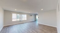 This single-floor residence offers a clean, modern aesthetic characterized by neutral tones, light-toned hardwood-style flooring, and crisp white baseboards throughout. The expansive open living area is a standout feature, bathed in natural light streaming through large sliding windows that frame outdoor views. Recessed lighting and a ceiling fan add functional comfort, while a wall-mounted air conditioning unit ensures climate control year-round.

The kitchen is designed for efficiency, featuring white cabinetry, light stone-look countertops, and stainless steel appliances including a gas range and dishwasher. Light tile flooring grounds the space with a clean, practical finish.

The bedrooms are generously proportioned, each featuring the same hardwood-style flooring found throughout the home. Mirrored sliding closet doors add depth and practicality to the sleeping quarters, while windows allow for ample natural light.

The bathroom is thoughtfully finished with large-format beige wall tiles surrounding a full soaking tub and shower combination. A recessed mosaic tile niche provides a refined storage detail, complemented by sliding glass shower doors and polished chrome fixtures.

Overall, the space presents a cohesive, well-maintained interior with a light and airy ambiance suited to a comfortable, contemporary lifestyle.