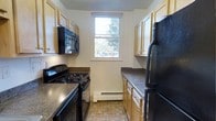 This 2-bedroom, 1-bathroom residence is laid out on a single floor, offering a straightforward and functional living arrangement. The kitchen is a standout feature, designed in a classic galley style that maximizes efficiency within the space. Light wood cabinetry lines both sides of the kitchen, providing generous storage, while dark granite-style countertops offer a contrasting visual appeal. Black appliances — including a gas range, over-the-range microwave, and a full-size refrigerator — are neatly integrated into the layout. A centrally positioned window above the baseboard heater allows natural light to filter in, brightening the kitchen and offering a pleasant view of surrounding greenery. The flooring features a warm, earth-toned tile pattern that complements the overall color palette of the space. The unit's two bedrooms provide comfortable living quarters, while the single bathroom serves the home's needs. The overall design of the unit emphasizes practicality and functionality, making it a well-suited space for those seeking a comfortable and organized home environment.