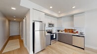 Located at 2700 W Cobalt Dr in Meridian, Idaho, this single-floor residence offers a clean, modern aesthetic throughout its open layout. The kitchen is a standout feature, showcasing a two-tone design with crisp white upper cabinetry and charcoal gray lower cabinets, all complemented by light quartz countertops and a white tile backsplash. A full suite of stainless steel appliances — including a refrigerator, electric range, over-the-range microwave, and dishwasher — provides a fully equipped and functional cooking space. A sliding barn door adds a stylish architectural accent near the kitchen entry. Light wood-tone flooring runs continuously throughout the unit, lending warmth and visual cohesion to the space. The living area is bright and open, with a bank of three large windows fitted with white horizontal blinds that allow ample natural light while framing views of the surrounding Meridian landscape. The neutral wall palette throughout the unit creates a versatile backdrop suited to a variety of interior styles. Recessed lighting in the kitchen ensures well-lit functionality, while the overall layout provides a sense of openness and ease of movement. This residence combines contemporary finishes with practical design, making it a well-appointed space in the Meridian community.