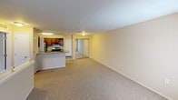 This single-floor residence offers a practical and well-organized layout designed for comfortable everyday living. The open-concept living area is generously sized, featuring neutral-toned carpet throughout, warm beige walls, and multiple windows dressed with vertical blinds that allow ample natural light to fill the space. A partial wall with a breakfast bar counter transitions the living area into the kitchen, creating a connected yet defined flow between spaces.

The kitchen is efficiently designed with rich medium-toned wood cabinetry, a stainless steel refrigerator, a gas range with stainless steel finish, a built-in overhead exhaust hood, and a double-basin sink set into a laminate countertop. Tile flooring in the kitchen provides a practical contrast to the carpeted living spaces. A pantry or utility closet is conveniently located adjacent to the kitchen area.

The bedroom is well-proportioned, featuring the same soft carpeting, a window for natural light, and access to a closet. A hallway connects the bedroom to the full bathroom, which includes a tub and shower combination with clean white tile surround, chrome fixtures, and a vanity with wood cabinetry. The unit presents a clean, move-in ready environment with a cohesive neutral color palette throughout.