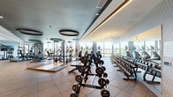 Located at 251 NJ-18 S in East Brunswick, New Jersey, this expansive fitness center offers a comprehensive workout facility spread across a single, generously sized floor. The space is divided into two distinct exercise rooms and a living area, each thoughtfully designed to support a wide range of fitness activities.

The main exercise room is a standout, featuring dramatic dark ceiling panels adorned with large circular LED light fixtures that lend a sleek, modern aesthetic. Floor-to-ceiling windows flood the space with natural light and offer open outdoor views, while wall-to-wall mirrors amplify the sense of scale. The room is fully equipped with power racks with platform flooring, cable machines, a full dumbbell rack, treadmills, and a variety of strength and cardio equipment — all set on durable rubber flooring.

A secondary exercise room provides a more intimate setting for functional training and group classes. It features full-length mirrors, mounted flat-screen TVs, TRX suspension trainers, yoga mats, and large glass doors that connect seamlessly to the main floor.

The living room area serves as a transitional lounge space, bathed in natural light from expansive sliding glass doors that open to outdoor views. Throughout, the facility maintains a cohesive, upscale design with patterned accent walls, recessed and linear lighting, and a clean, modern finish that creates a motivating and professional environment.