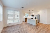 Located at 105 NE Sixth Ave in vibrant Delray Beach, Florida, this single-story, 3-bedroom, 2-bathroom home offers a clean, modern aesthetic throughout. The open-concept living and kitchen area serves as the heart of the home, featuring light wood-look flooring, crisp white walls, and an abundance of natural light streaming through large windows dressed with slatted blinds. The kitchen is thoughtfully designed with white shaker-style cabinetry, quartz countertops, a central island with built-in shelving, stainless steel appliances including a refrigerator, range, microwave, and dishwasher, and sleek pendant lighting overhead. A door off the kitchen provides convenient outdoor access. The hallway, accented with louvered closet doors, connects the main living area to the three bedrooms, each finished with the same warm wood-look flooring, neutral paint, and windows that invite natural light. The spacious primary bedroom includes a ceiling fan and dedicated closet space. Both bathrooms are finished to a high standard, with one featuring a glass-enclosed walk-in shower with large-format tile, a dual-sink vanity with white cabinetry, quartz countertops, and matte black hardware accents throughout. Two additional closets provide ample storage across the home.